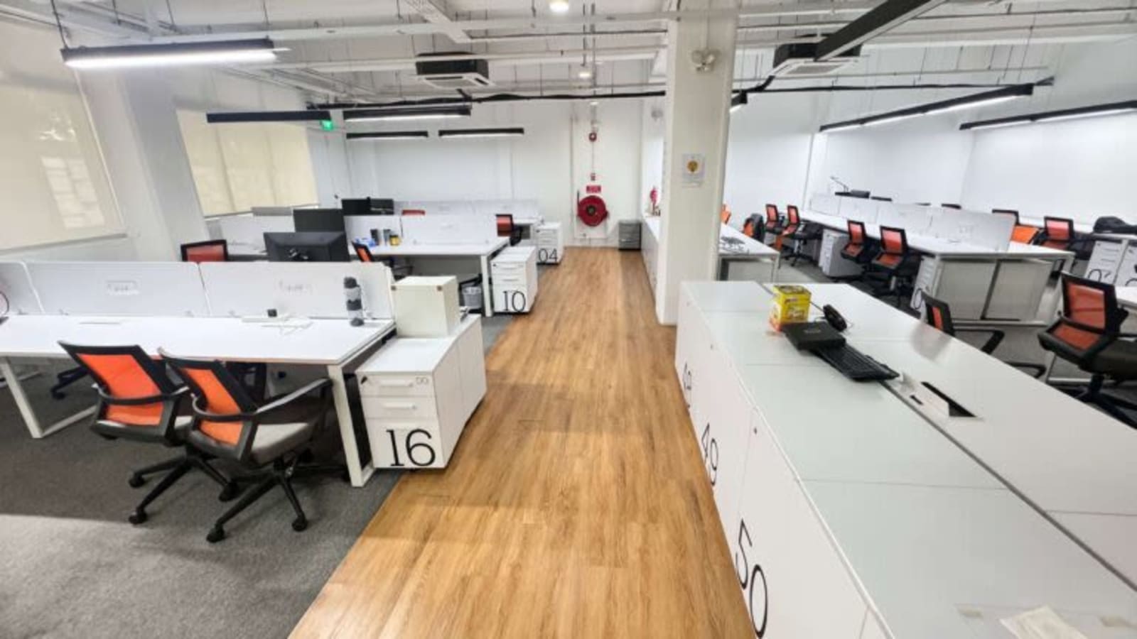 Bright, open coworking area with modern desks and vibrant orange chairs. Ideal for collaboration.