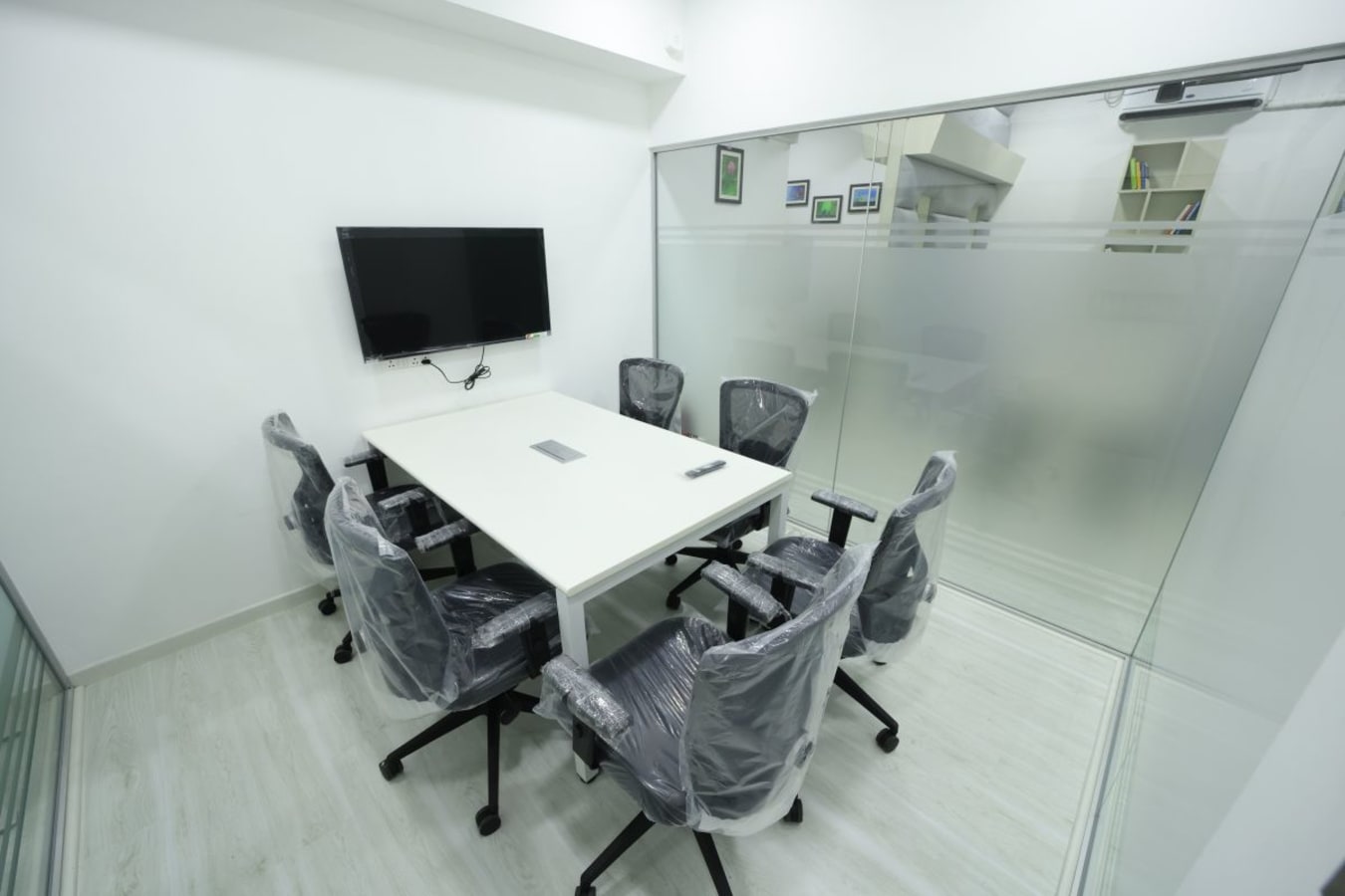 Sleek meeting room with glass walls, equipped with a TV and ergonomic chairs. Ideal for productive sessions.
