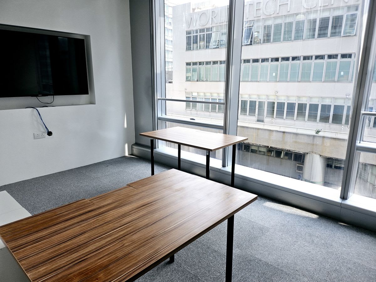 Bright coworking space with large windows, modern desks, and a wall-mounted screen. Ideal for productivity.