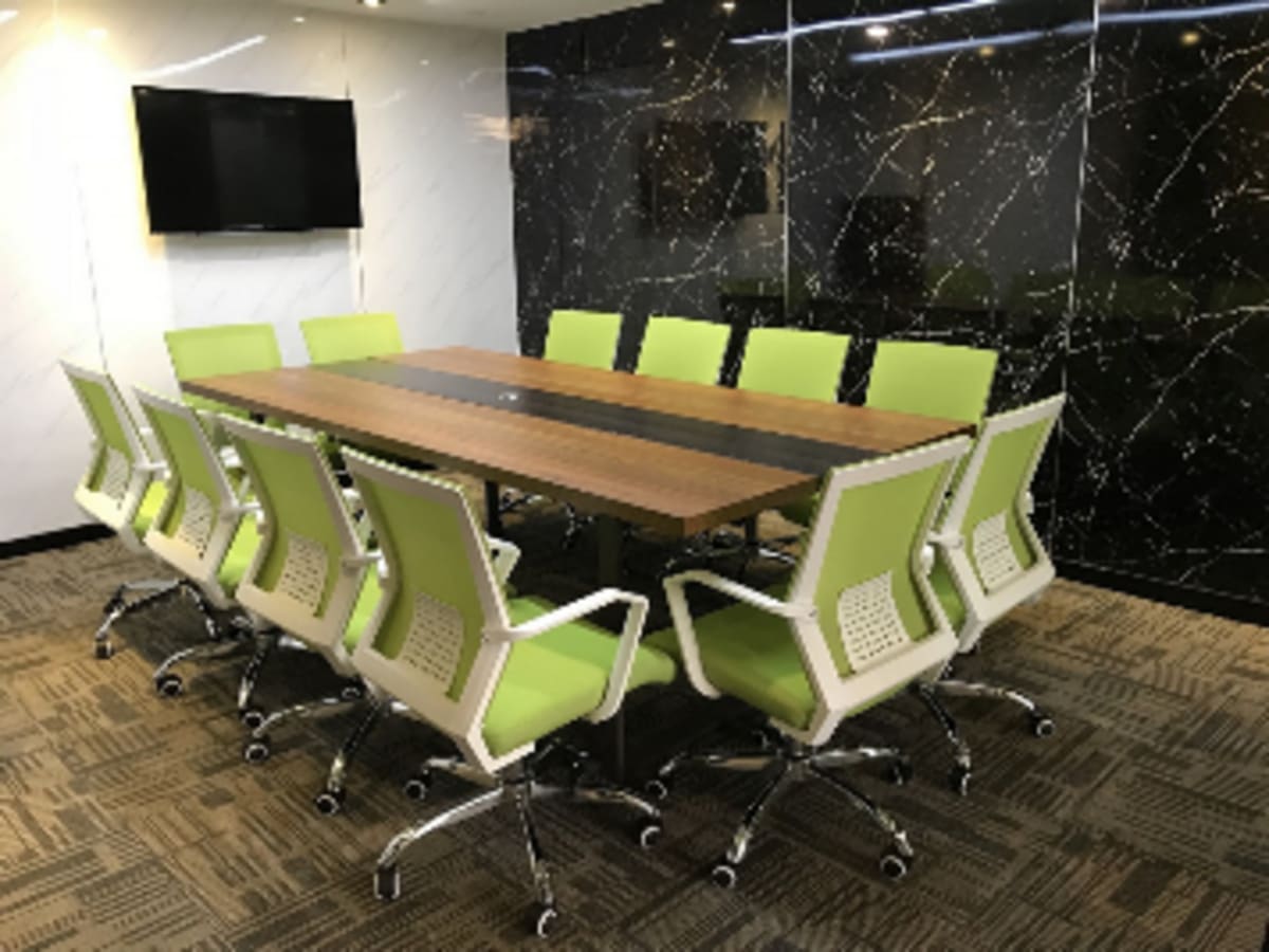 Modern meeting room with bright green chairs, wood table, marble accents, and a wall-mounted TV.