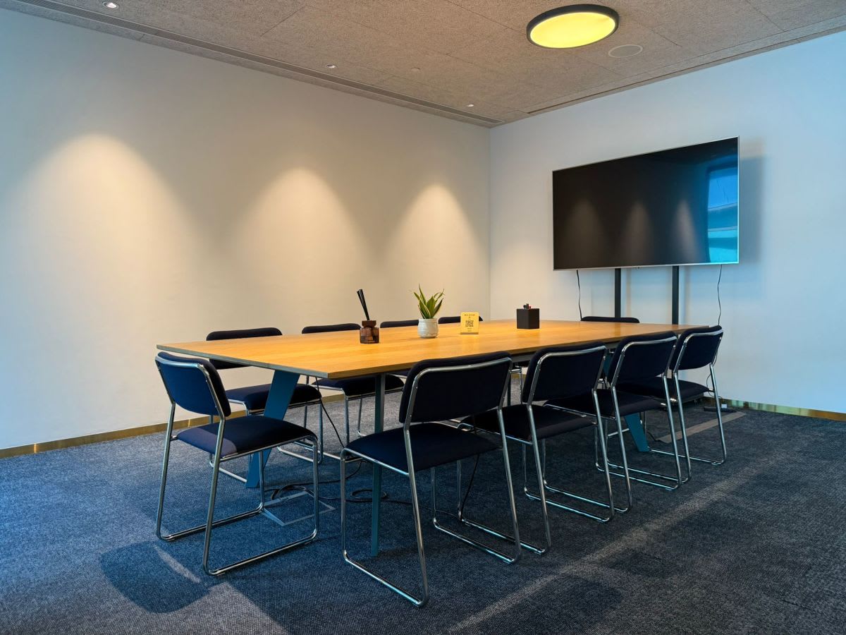 Modern meeting room with ample seating, sleek table, and large screen. Ideal for collaboration.