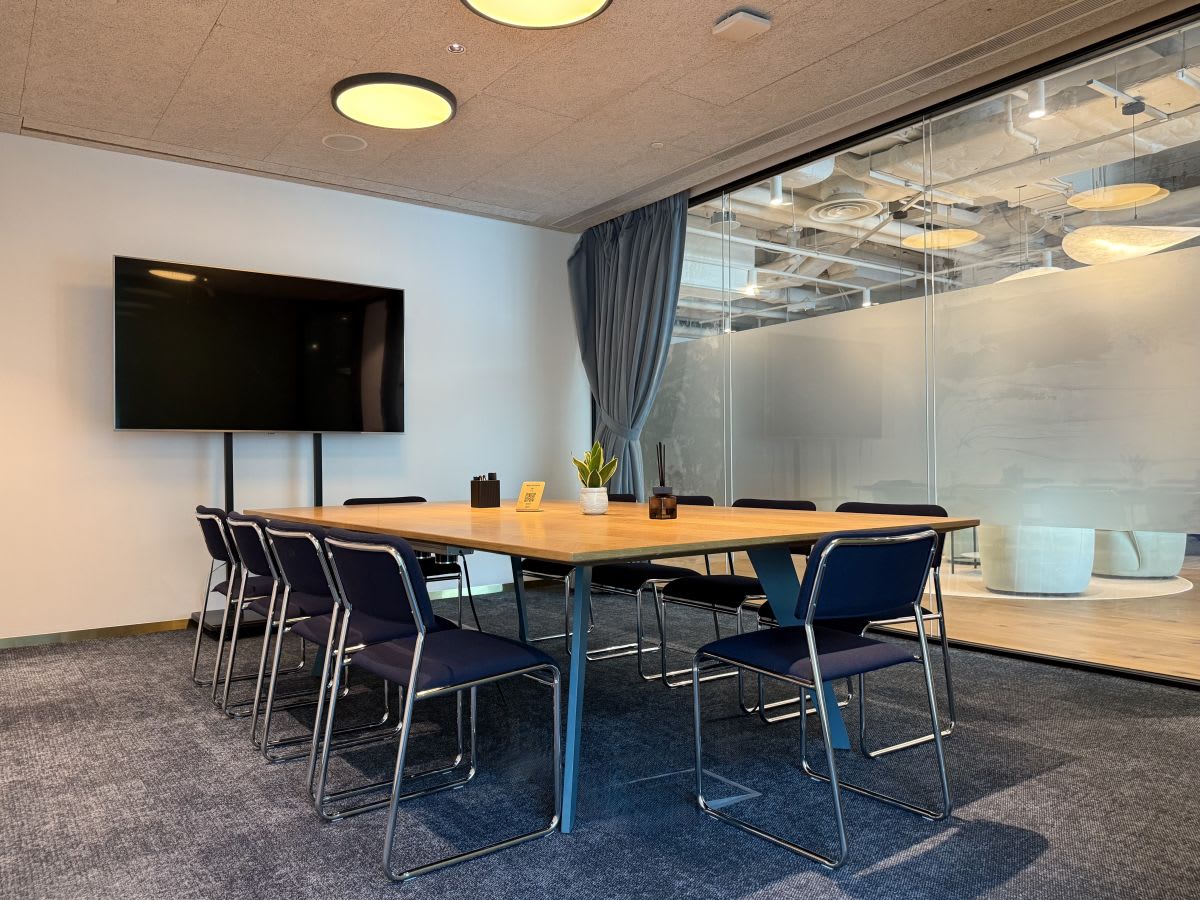 Modern conference room with seating for eight, large screen, and glass partition in a stylish coworking space.