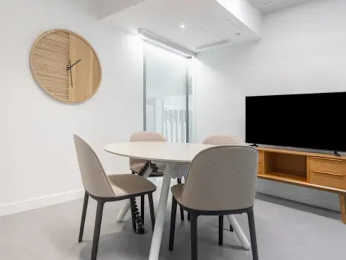 Modern coworking space with round table, comfortable seating, and a sleek TV setup.