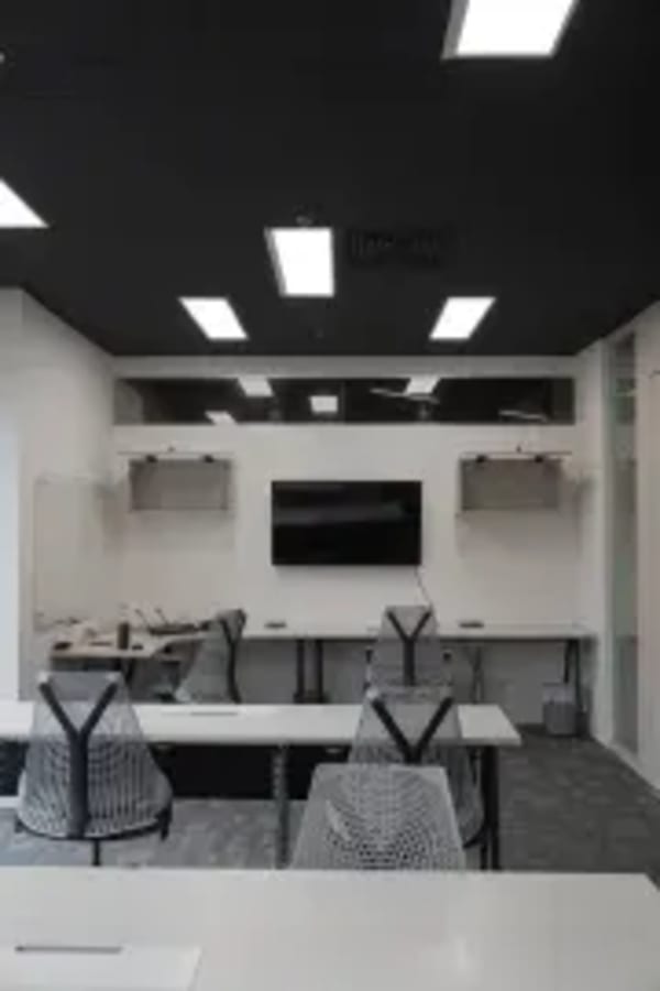 Modern coworking space with sleek desks, ergonomic chairs, and a central screen for presentations.