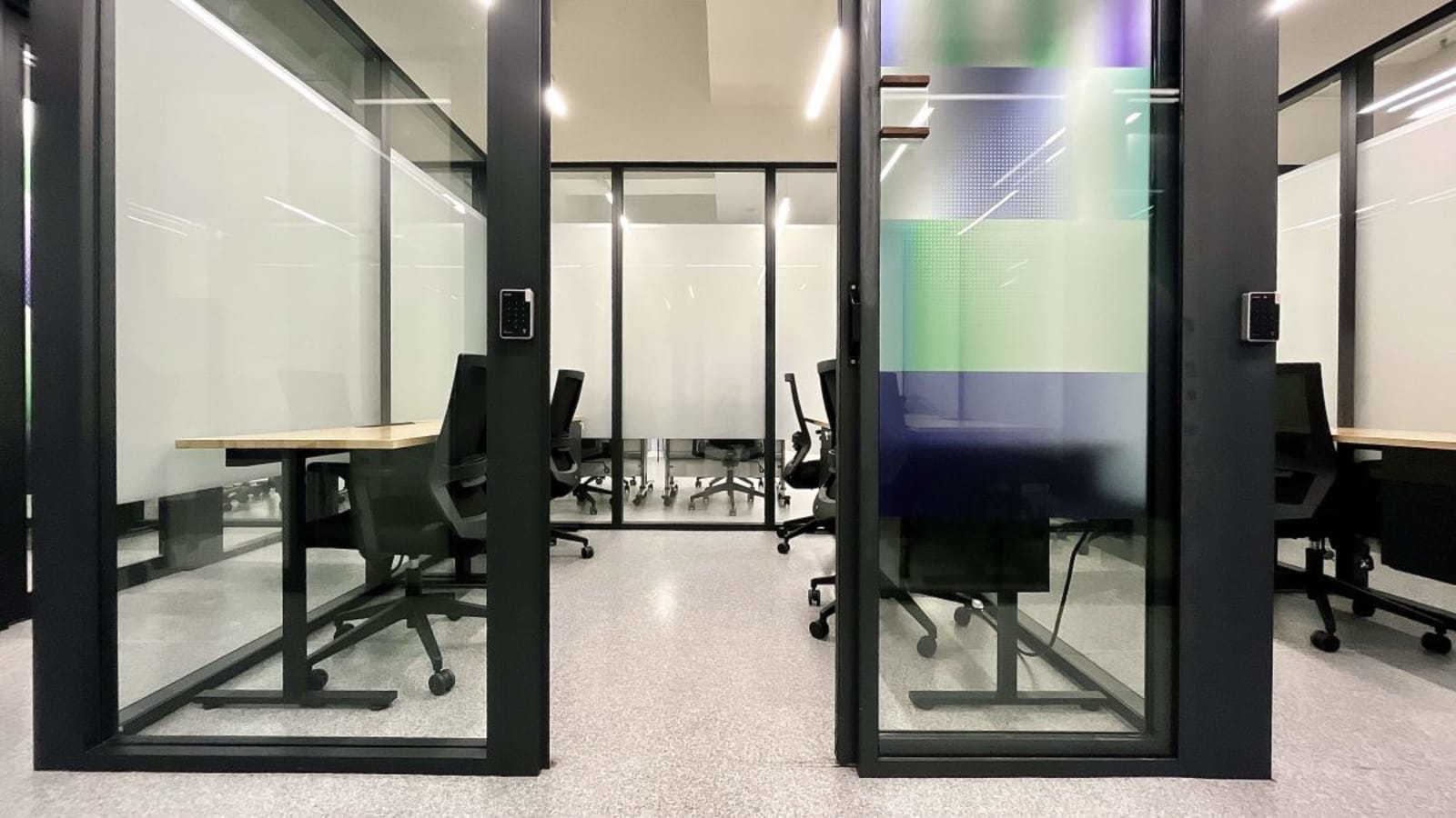 Modern glass-walled private offices with sleek furniture in a vibrant coworking space.
