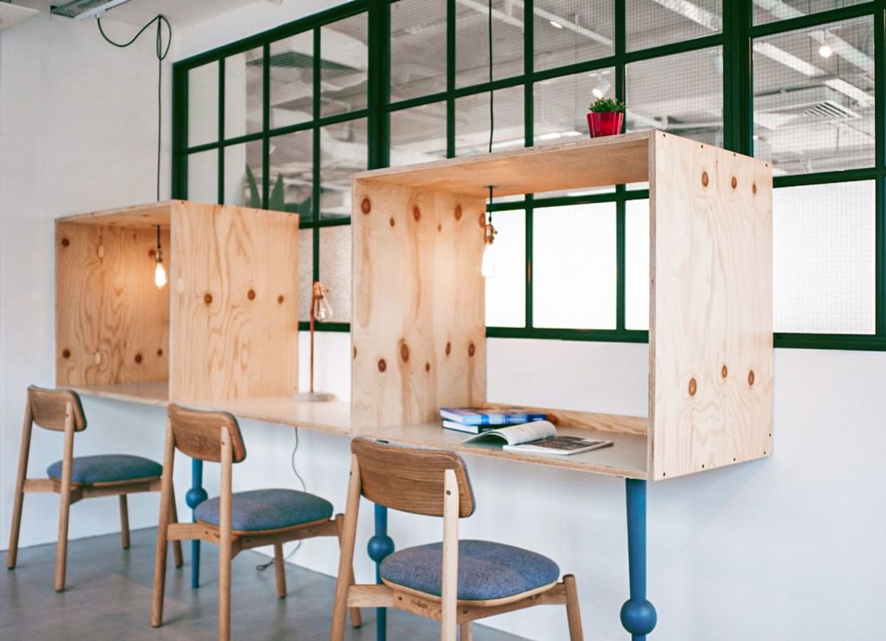 Modern coworking space with wood desks, cozy chairs, and vibrant lighting. Ideal for productivity.