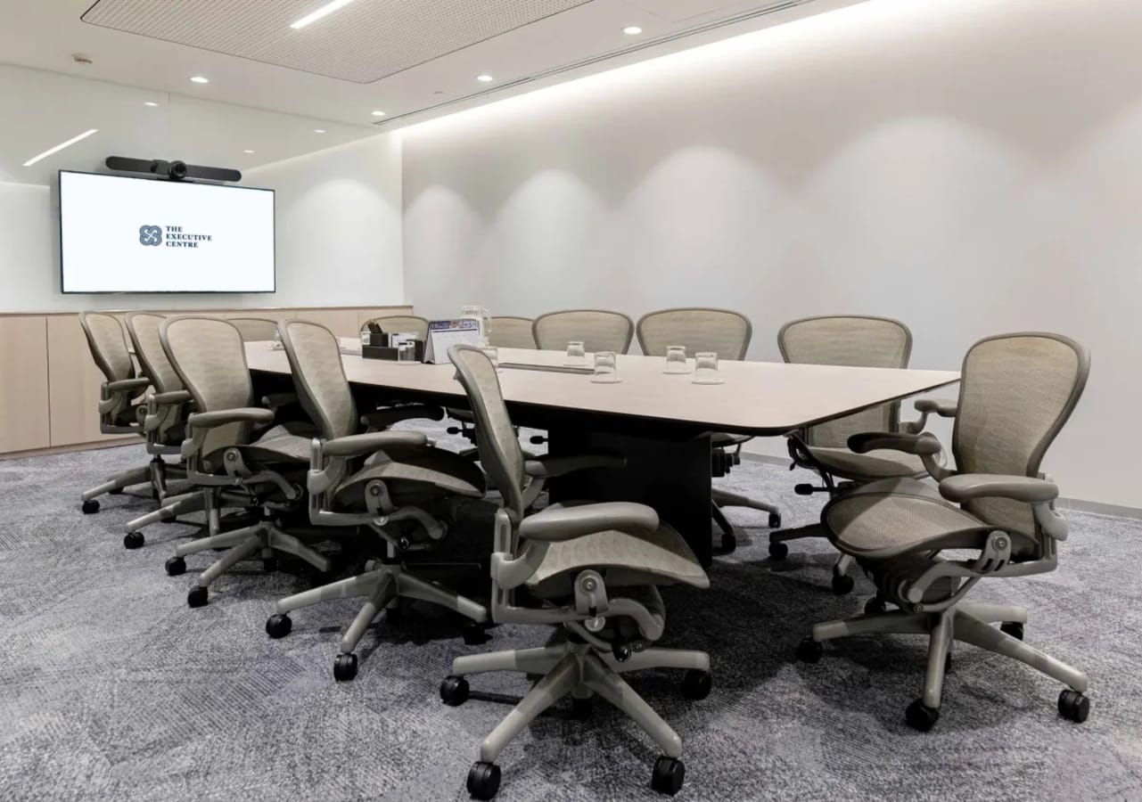 Modern conference room with ergonomic chairs, large table, and video conferencing screen. Perfect for team meetings.