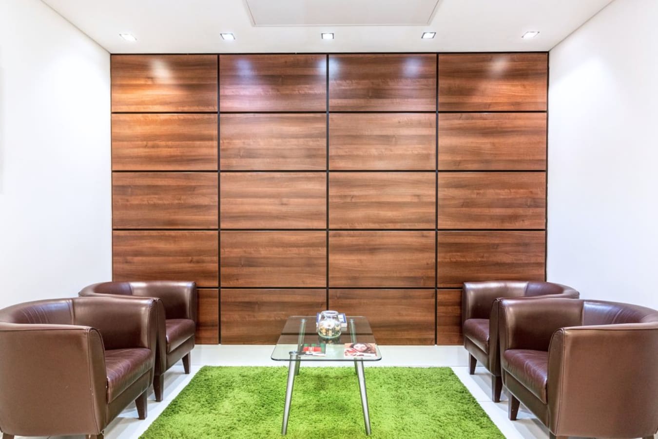 Stylish lounge area with sleek leather chairs, glass coffee table, and vibrant green rug. Ideal for meetings.
