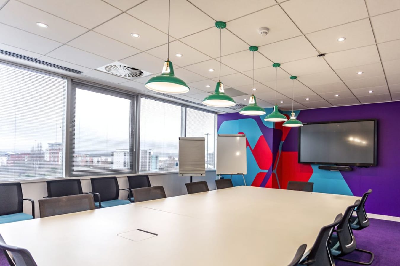 Vibrant meeting room with large table, modern lighting, and AV setup in Windsor Place coworking space.