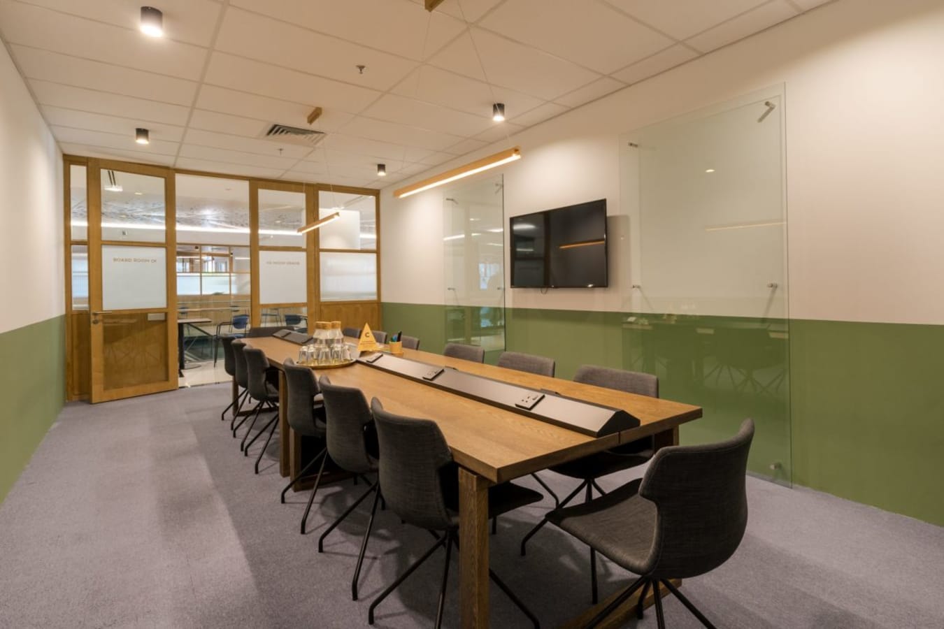 Modern meeting room with ample seating, sleek wood table, and smart TV for presentations.
