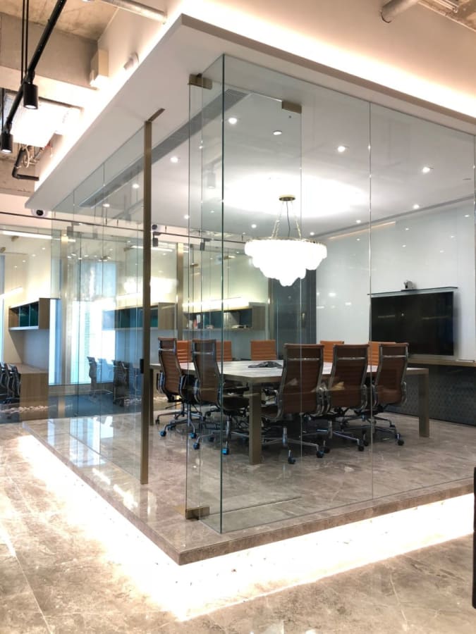 Modern glass-walled meeting room with elegant chandelier, ideal for dynamic coworking sessions.