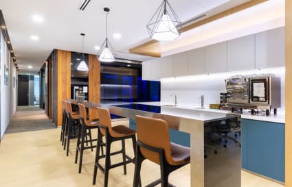 Modern coworking kitchen with sleek bar seating, stylish lighting, and coffee amenities.