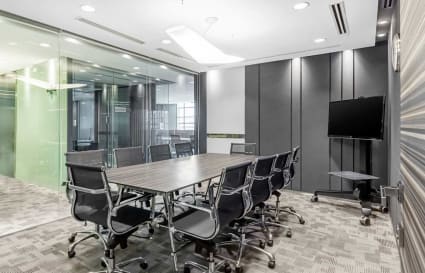 Modern conference room with sleek seating, large table, and AV setup. Glass walls enhance openness.