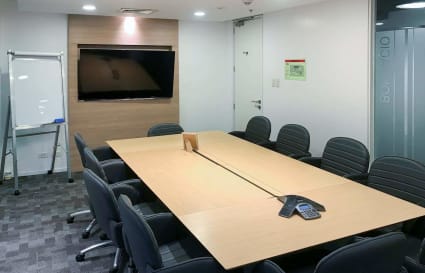 Modern meeting room with a large conference table, ergonomic chairs, and digital presentation screen.