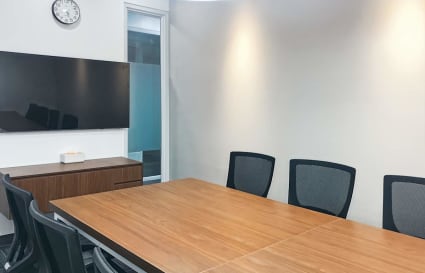 Modern meeting room with sleek wood table, ergonomic chairs, and a wall-mounted screen.