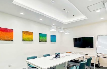 Modern meeting room with sleek white table, vibrant wall art, and ample lighting. Ideal for collaboration.