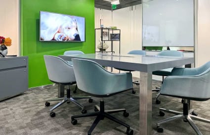 Modern meeting area with vibrant green accent wall, cozy seating, and digital display.
