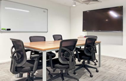 Modern meeting area with sleek furniture, large screen, and whiteboard. Ideal for collaboration.
