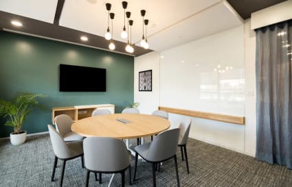 Modern coworking room with a round table, seating for six, and a whiteboard, under stylish lighting.