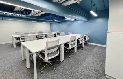 Modern coworking space with ample seating, sleek white desks, and vibrant blue accents.