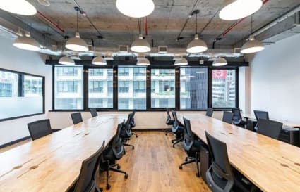 Modern coworking space with large wooden desks, ergonomic chairs, and ample natural light.