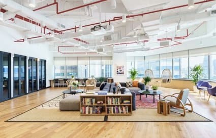 Bright and modern coworking area with open seating, bookshelves, and panoramic city views.