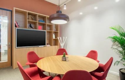 Modern coworking area with a round table, red chairs, ample shelving, and accent lighting.