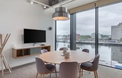 Bright coworking space with round table, modern lighting, and scenic waterfront view.