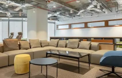 Modern coworking lounge with ample seating, sleek tables, and industrial ceiling design.