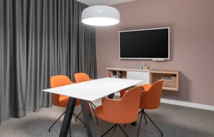 Modern meeting area with sleek table, vibrant chairs, and a wall-mounted TV, ideal for collaboration.