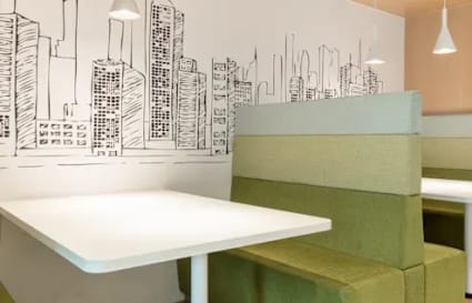 Modern coworking space with cozy booth seating and artistic cityscape wall art.