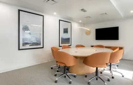 Modern meeting room with a round table, cozy chairs, and a large screen for presentations.