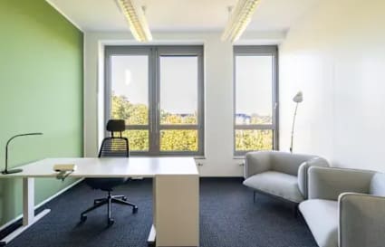 Modern coworking space with natural light, contemporary furniture, and a serene green accent wall.