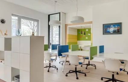 Bright coworking area with modern desks, colorful partitions, and ample natural light.