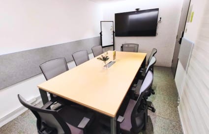 Modern meeting room with seating for eight, equipped with a large screen and whiteboard.