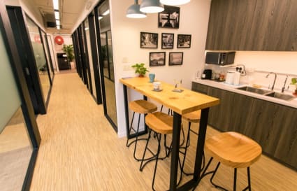 Bright coworking kitchen with wooden high-top table and stools, perfect for quick breaks.