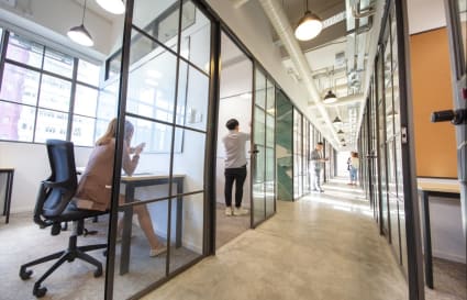 Modern coworking space with private glass offices, abundant natural light, and a collaborative atmosphere.