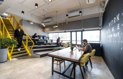 Modern coworking space with open seating, vibrant yellow stairs, and abundant natural light.
