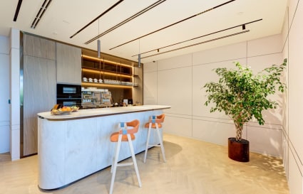 Modern kitchen area with sleek countertops, stylish bar stools, and lush greenery. Perfect for breaks!