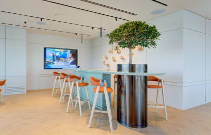Modern coworking space with stylish seating, greenery, and a large TV for presentations.