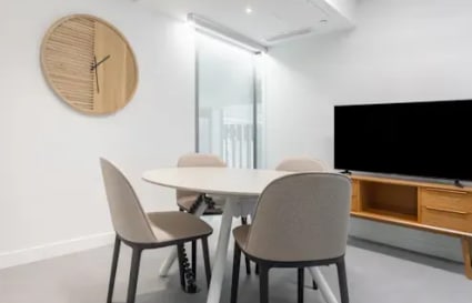 Modern coworking space with round table, comfortable seating, and a sleek TV setup.