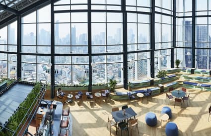 Bright coworking space with panoramic city views, modern seating, and abundant natural light.