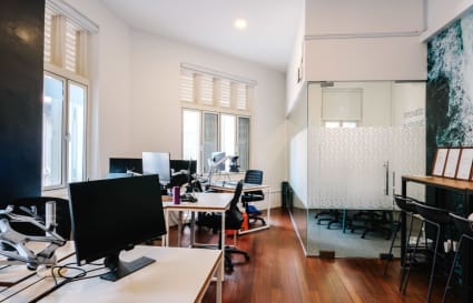 Open-plan coworking space with ample natural light, modern desks, and a private meeting room.