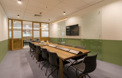 Modern meeting room with ample seating, sleek wood table, and smart TV for presentations.