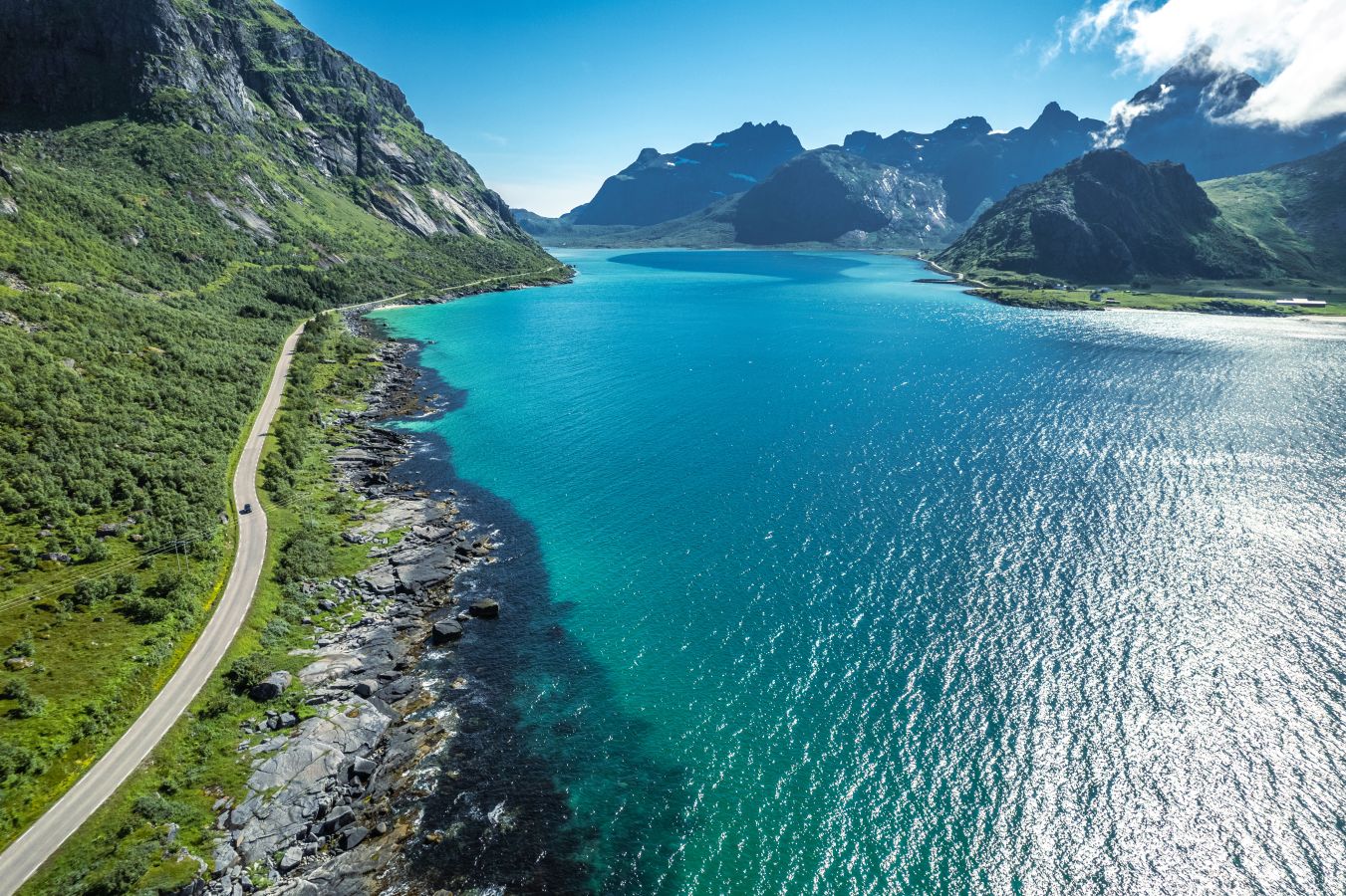 En bilvei ved en nydelig isblå innsjø, med fjell i horisonten, i Nordland Norge Norway