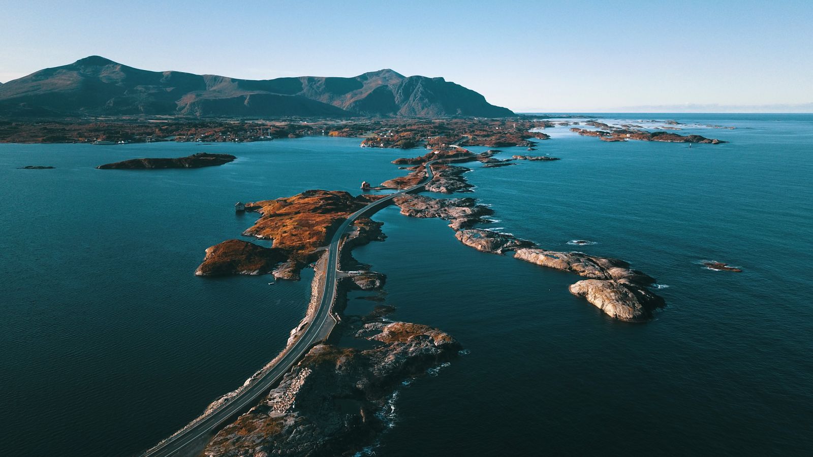 Et luftfoto av en Atlanterhavsvegen som snor seg over broer og små øyer gjennom et vakkert norsk kystlandskap med dypblått hav og fjell i bakgrunnen, i Møre og Romsdal, Norge Norway.