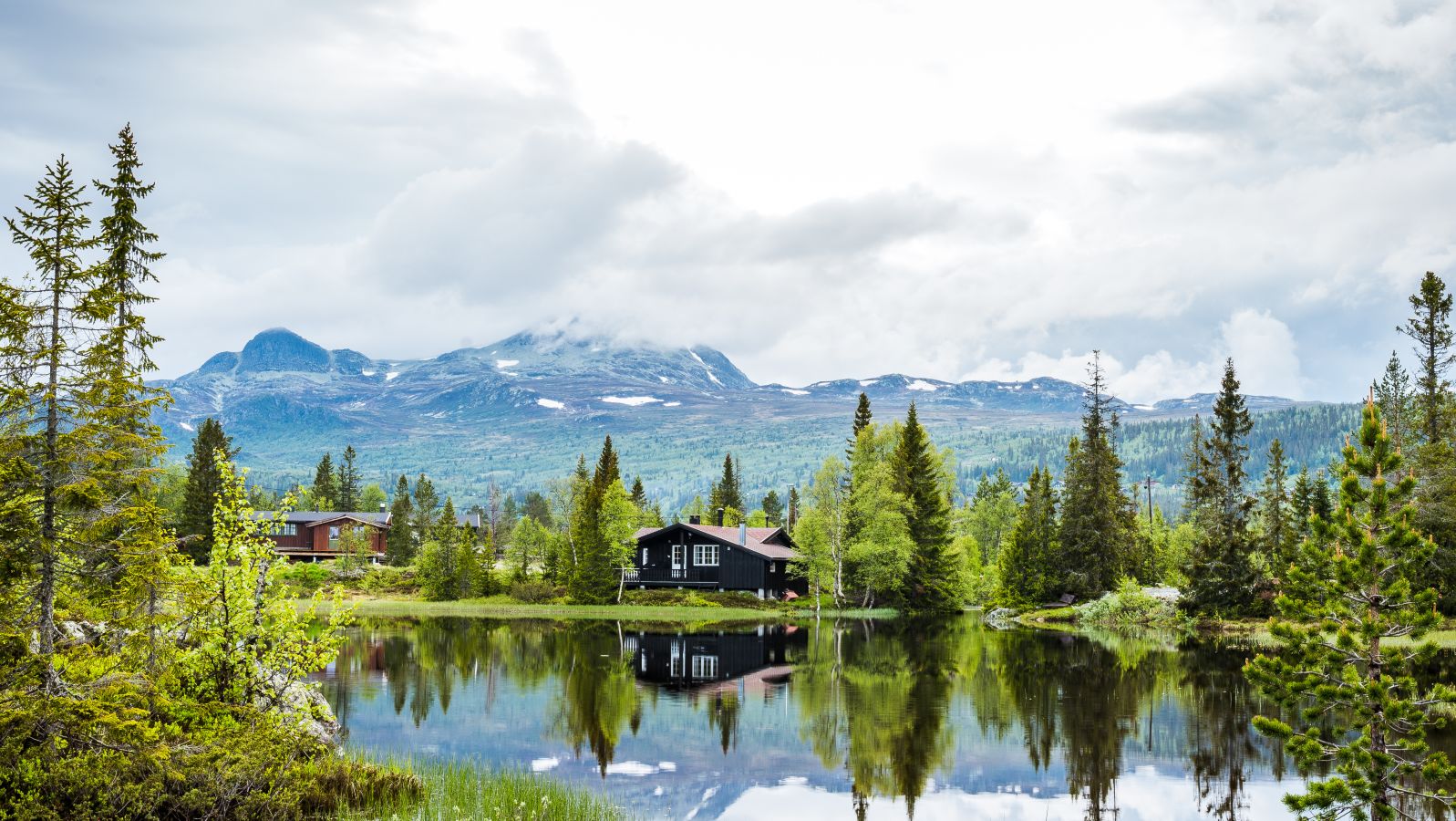 Et fotografi av en klassisk norsk hytte ved en liten innsjø i vakre Telemark Norge Norway, med fjell i bakgrunnen