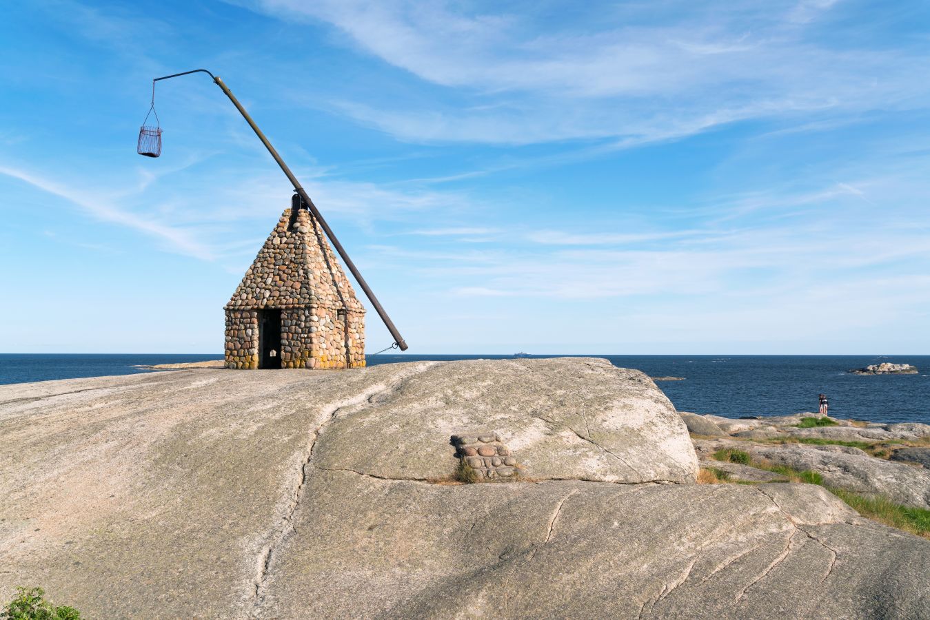 Det ikoniske vippefyret på Verdens Ende står plassert på blankskurte svaberg ved havet med blå himmel.