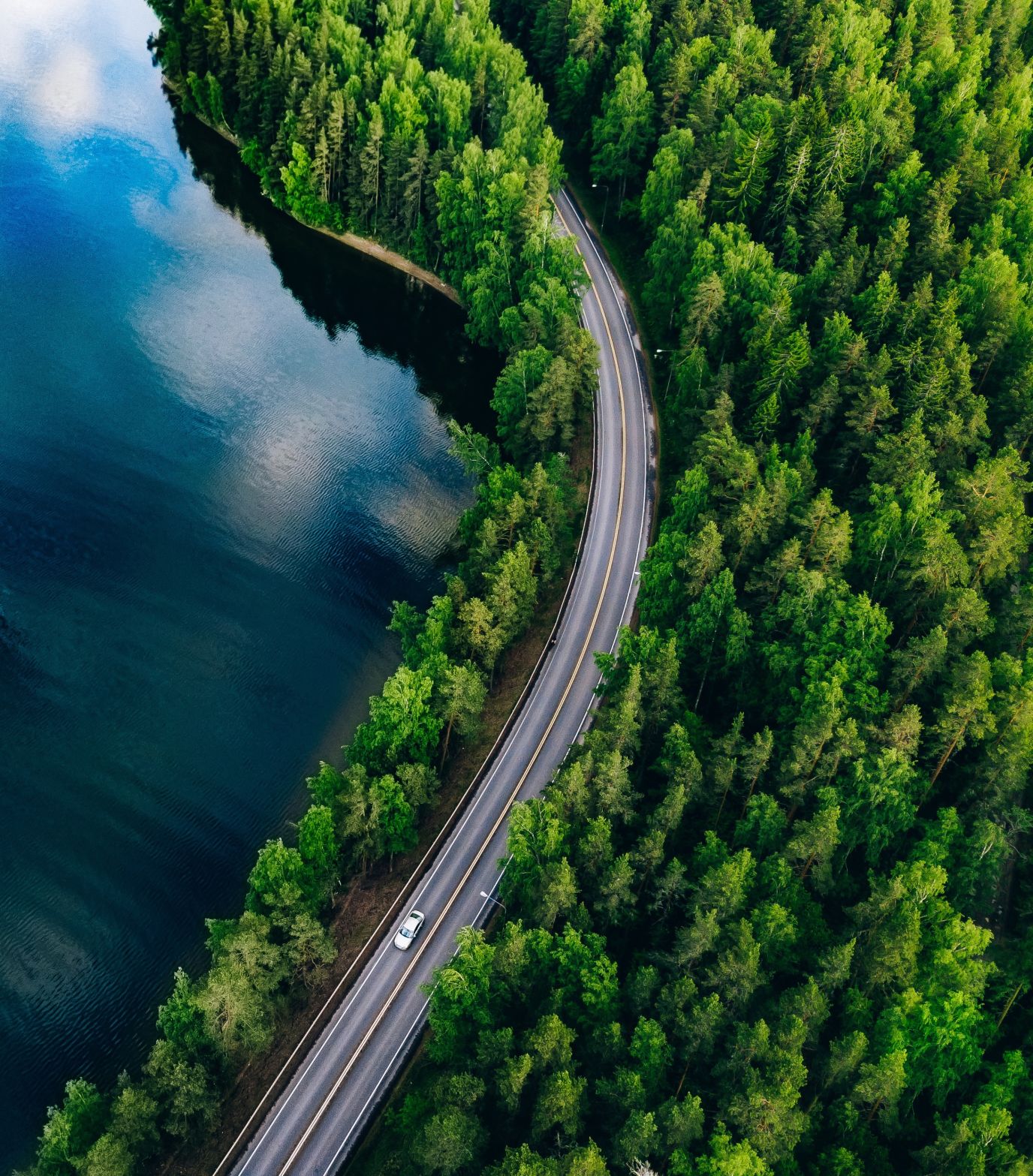 et vakkert naturlandskap med bilvei, skog og innsjø sett ovenfra