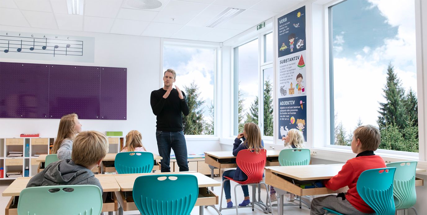 Et lyst klasserom med en mannlig lærer som forklarer noe til ivrige elever